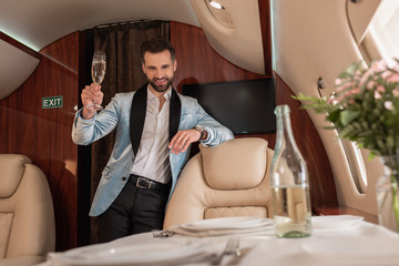 Wall Mural - selective focus of smiling, elegant man holding glass of champagne and looking at camera in private plane