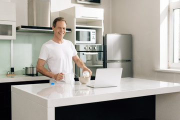 Wall Mural - happy freelancer holding bottle and pouring milk in bowl near laptop