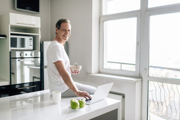 Wall Mural - happy freelancer holding bowl near cup, apples and laptop