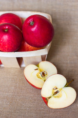 Red apples in a wooden basket box and two halves cut with seeds on a homespun linen napkin, summer healthy fruits vitamins, juicy dessert and snack