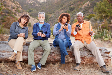 Group Of Senior Friends On Hike In Countryside Checking Mobiles Phones For Fear Of Missing Out