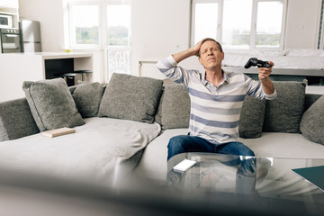 Wall Mural - KYIV, UKRAINE - APRIL 14, 2020: selective focus of upset man touching head and holding joystick near smartphone with white screen on coffee table