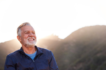 Portrait Of Smiling Hispanic Senior Man Outdoors In Countryside With Mountains In Background