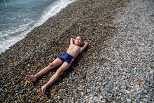 Boy Resting On A Pebble Beach By The Sea