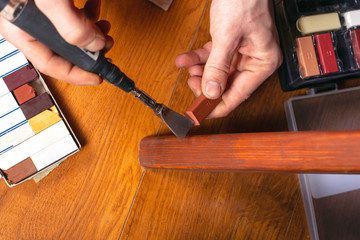 restoration of wooden furniture. master fixes a scratch on the table leg with a wax pencil and a soldering iron close-up