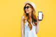 © Shopping King Louie - Happy girl in a summer hat shows a blank screen mobile phone for copy space, on a blue background