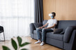 © LIGHTFIELD STUDIOS - Selective focus of man in vr headset and medical mask sitting near laptop on couch in living room