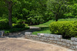 Low granite block wall, path through an urban park in spring, green landscape with creative copy space, horizontal aspect