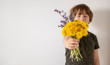 Uśmiechnięty chłopiec trzymający bukiet polnych kwiatów, białe tło.