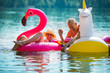 © Suzi Media  - Elderly couple having fun on inflatable flamingo and unicorn. Funny active pensioners happy together enjoying summer vacation on the beach in Europe, laughing, playing the fool, splashing water.