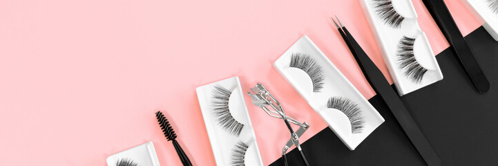 Various tools for eye lash extensions on a trendy pastel pink and black background. Banner. Concept. Eyelash curler, tweezers. Makeup accessories. Cosmetics. Fake eyelashes. Place for text. Top view.