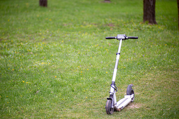 white electric scooter on a green lawn in summer. The concept of two-wheeled urban environmental transport.