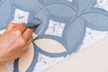 Stay At Home And Home Improvement Concept: Close Up And Top View Of A Hand Holding A Brush Is Painting A Decorative Template On The Floor Tiles Into Gray By Using A Vintage Pattern Stencil