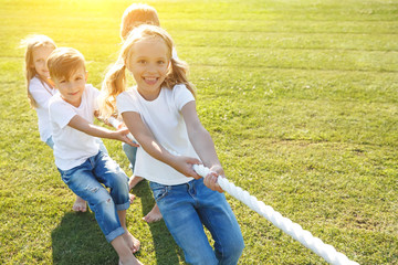 A group of children have fun playing in nature. Children jump over the rope. Warm summer evening with sunset light.