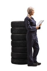 Poster - Female auto mechanic holding a document on a clipboard and standing next to a pile od tires