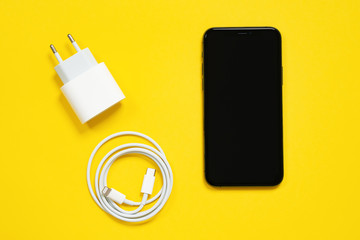 Wall Mural - May 01, 2020, Rostov, Russia: Smartphone Apple iPhone screen up, wrapped in a ring USB Lightning Cable and power adapter on yellow background, top view, copy space.