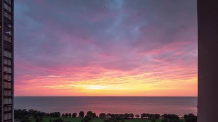 Wall Mural - Incredible panning down aerial timelapse of a yellow pink purple and blue sunrise reflects on the water of Lake Michigan as it rises over the horizon with traffic zooming by on Lake Shore Drive below.
