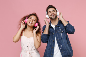 Wall Mural - Joyful young couple two friends european guy african american girl in casual clothes isolated on pastel pink background. People lifestyle concept. Listen music with headphones, keeping eyes closed.