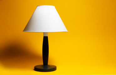 Close-up of night lamp with white shade and black tripod on background of orange color.