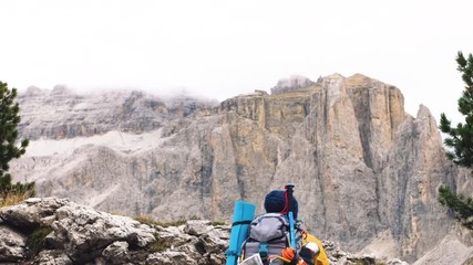 Wall Mural - young man hiker hiking up stone mountain with cloudy sky and fog. yellow jacket, backpack, black bea