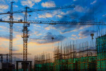 Tower crane and building construction site silhouette at sunrise.