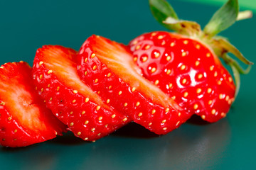 Wall Mural - Fruit background. Several slices of strawberries on a green background. Texture of strawberries. Close-up beautiful strawberry slices. Horizontal, close-up, nobody, side view. Concept of agriculture 