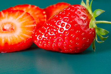 Wall Mural - Fruit background. One whole strawberry and several strawberry slices on a green background. Texture of strawberry berries. Beautiful berries close-up. Horizontal, close-up, nobody, side view. 