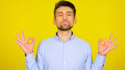 Handsome bearded man meditating with his eyes closed on a yellow background with copyspace. Guy in a light blue shirt. Place for text or product