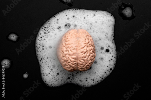 Brainwashing, lower critical thinking and mind control concept with human brain washing in soapy bubbles isolated on black background