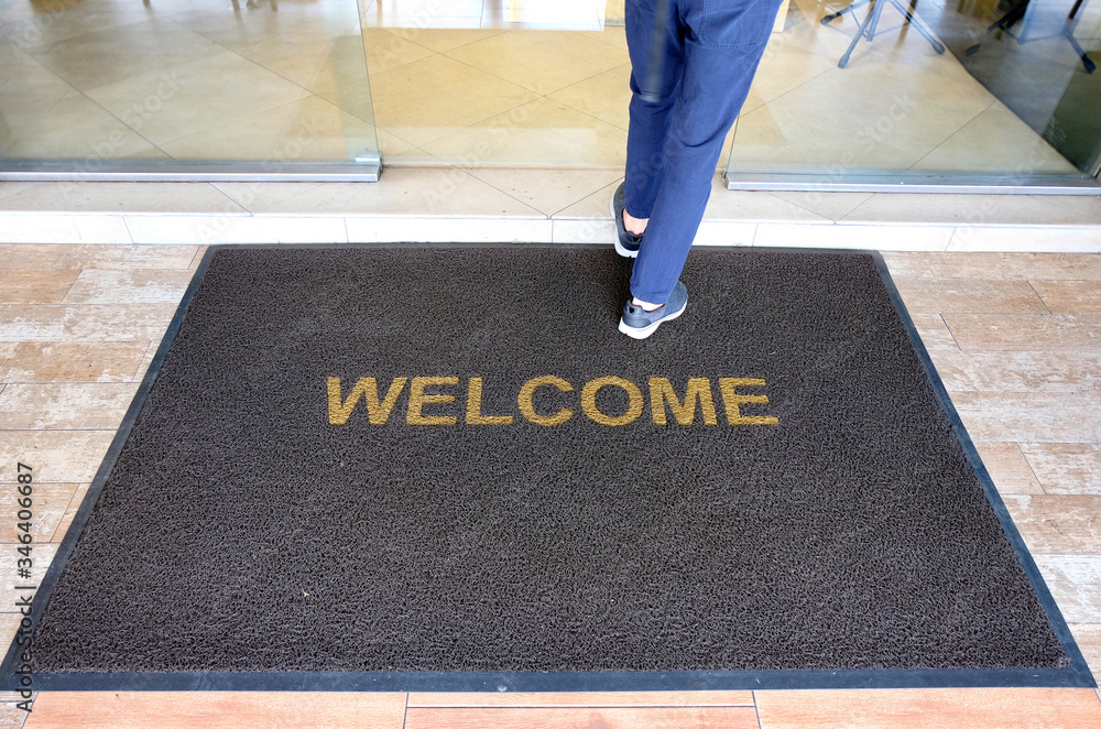 A welcome mat at the entrance of a cafe restaurant as a customer is seen entering through the front door. - obrazy, fototapety, plakaty 