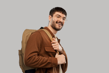 Wall Mural - travel, tourism and people concept - smiling young man in glasses with backpack over grey background