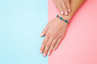 Flower bracelet on young woman hand wrist. Pink and blue table background. Pastel color. Closeup. Top down view. Two sides.