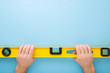 Man hands holding yellow spirit level on light blue table background. Building tool for floor, wall, ceiling or other surfaces level precision. Point of view shot. Empty place for text. Top down view.