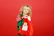 © Serenkonata - Little girl in Santa elf helper costume on bright red vivid color background.