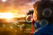 Little boy playing with bubble wand blowing soap bubbles in summer sunshine