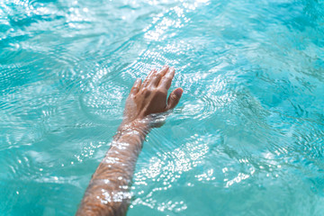  Tender touching surface of sea water. Woman's hand touching surface of turquoise water in sunlight. Nature water concept, woman hand.