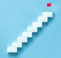 concept to achieve the goal, the upward movement. white staircase with a red flag on the top step on