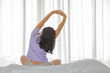 © Akarawut - Back of woman stretching after wake up in her bedroom looking out at the urban city view