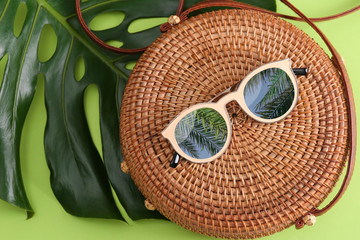 Bamboo bag and sunglasses with reflection of palm trees on green background, flat lay