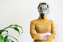 Horizontal View Of Woman With Gas Mask Surrounded With Plants At Home Isolated On White Background. Conceptual Idea Of Greenhouse Effect In Ecosystem. Quarantine At Home Covid 19 Coronavirus Concept.