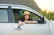 © pangoasis - Young happy woman wearing yellow hat out of white SUV car window while roadtrip, Travel car in vacation