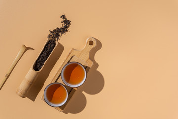 Wall Mural - Two ceramic bowls with black puer tea ,dry pu-erh tea leaves in a wooden bamboo spoon on a beige background, tea background.