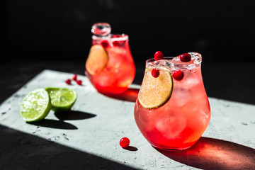 Wall Mural - Cranberry tonic with lime in beautiful glasses, grey background, direct natural light, horizontal photo