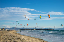 Kitesurfing In Tarifa. Plenty Of Colorful Kites Flying Against A Background Of The Mountains, Beautiful Clouds And Waves Of The Atlantic Ocean