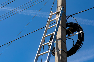 A metal staircase next to a concrete electric pole with a lot of wires against the blue sky. Preparation for electrical work.