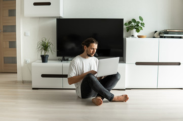 Man with beard, working at home on project with a laptop in front of him or speaking with a friends or business partners or clients via webcam and sitting on a floor. Freelancer working from home.