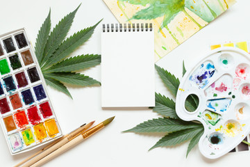 Set of watercolor paints, art brushes, palette and blank album. Marijuana leaf. Cannabis reveals creativity. The concept of art.