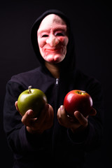 Wall Mural - Portrait of young man with hoodie and horror mask holding apples