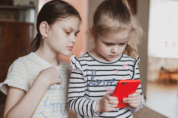 Happy little girls with a smartphone in hands communicate at home with loved ones using modern technology