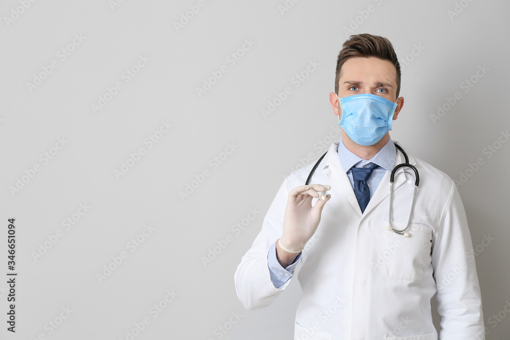 Male doctor with flashlight on grey background